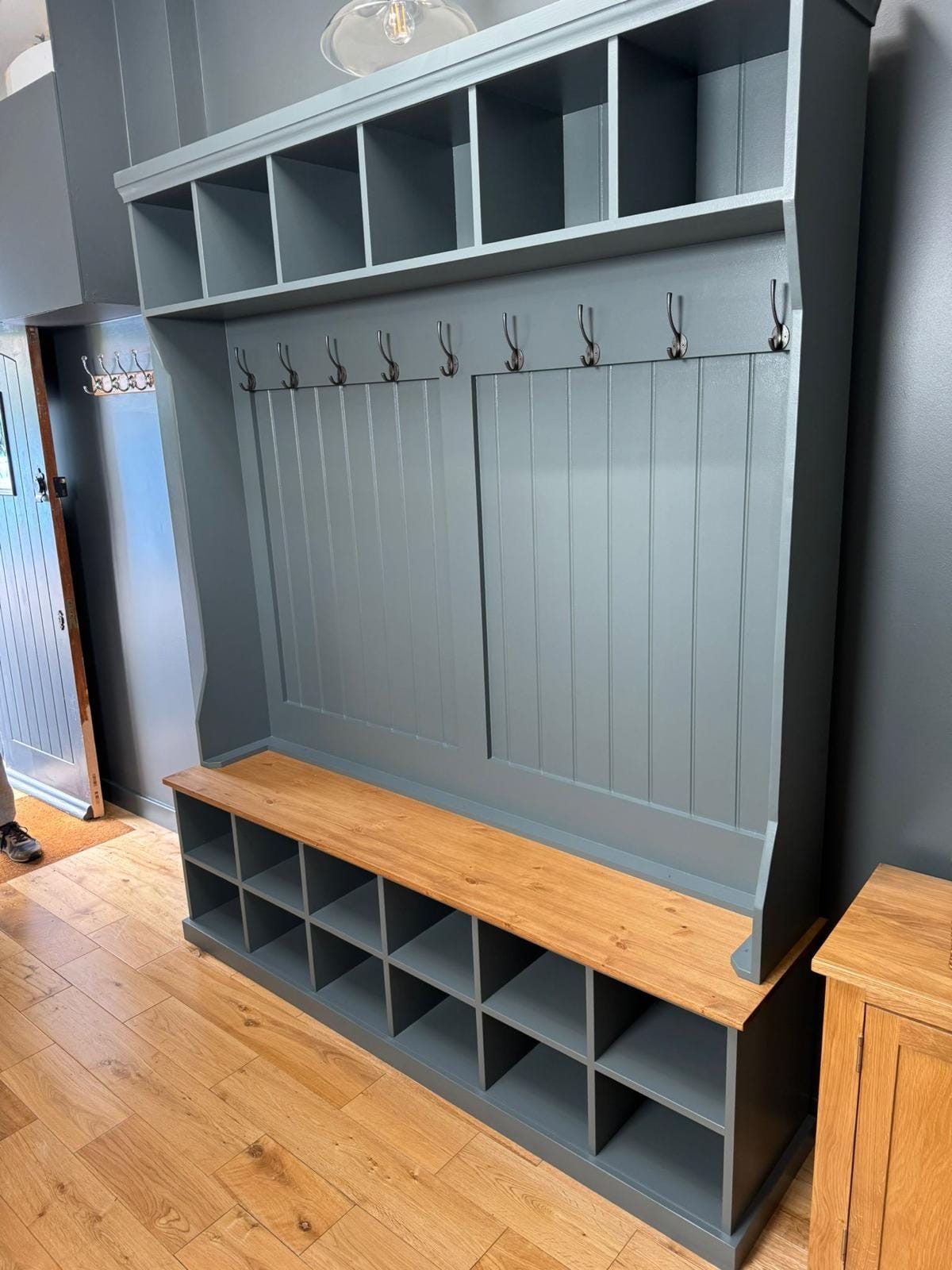 Grey-blue hall stand with coat hooks, cubbies and bench, installed in a home